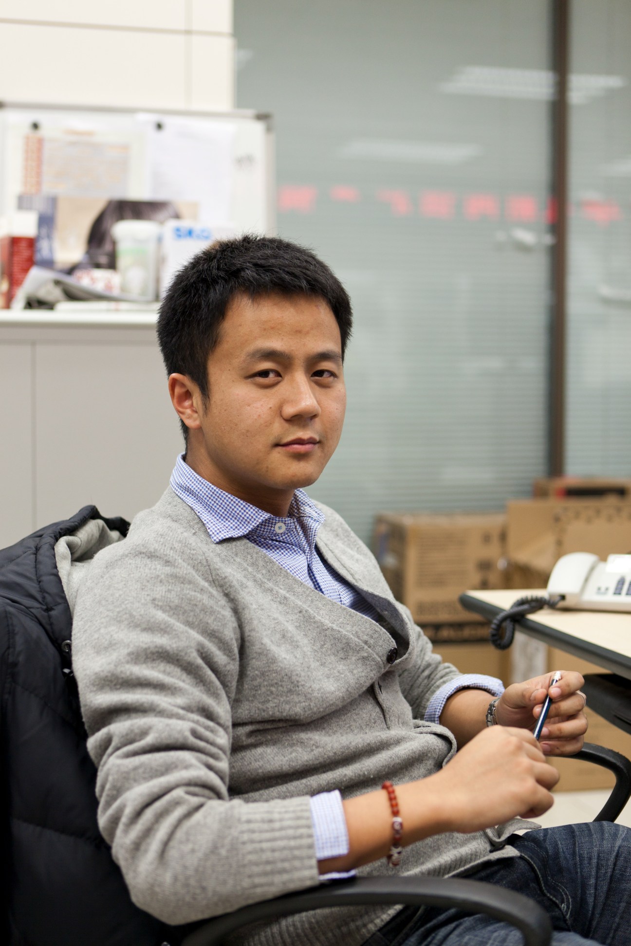 Tao Ye, CNC correspondent, sits in an office holding a pen while looking at the camera.