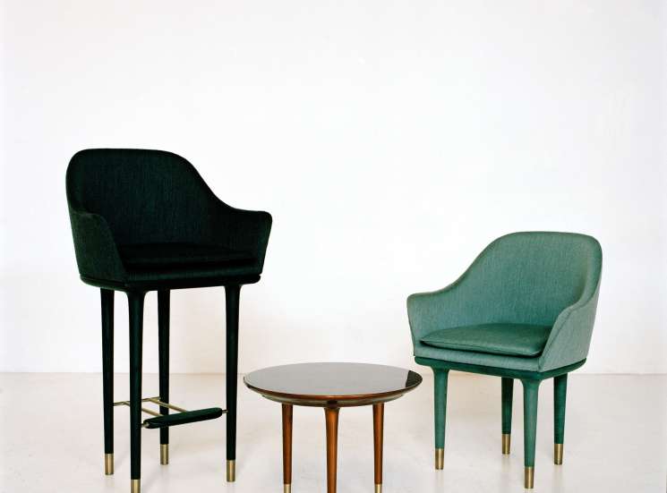 Two upholstered chairs in black and green wool with brass-tipped legs flanking a small round wooden table.