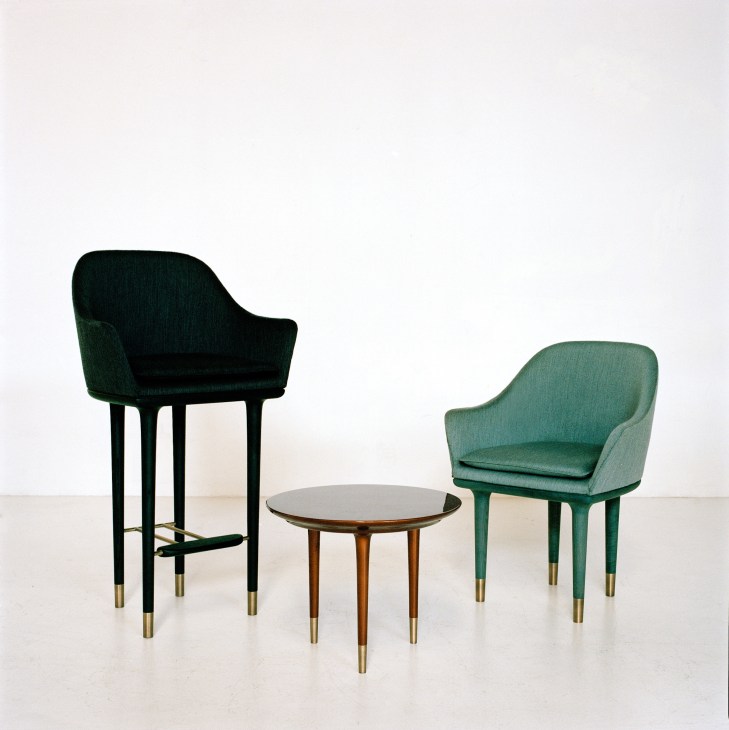 Two upholstered chairs in black and green wool with brass-tipped legs flanking a small round wooden table.