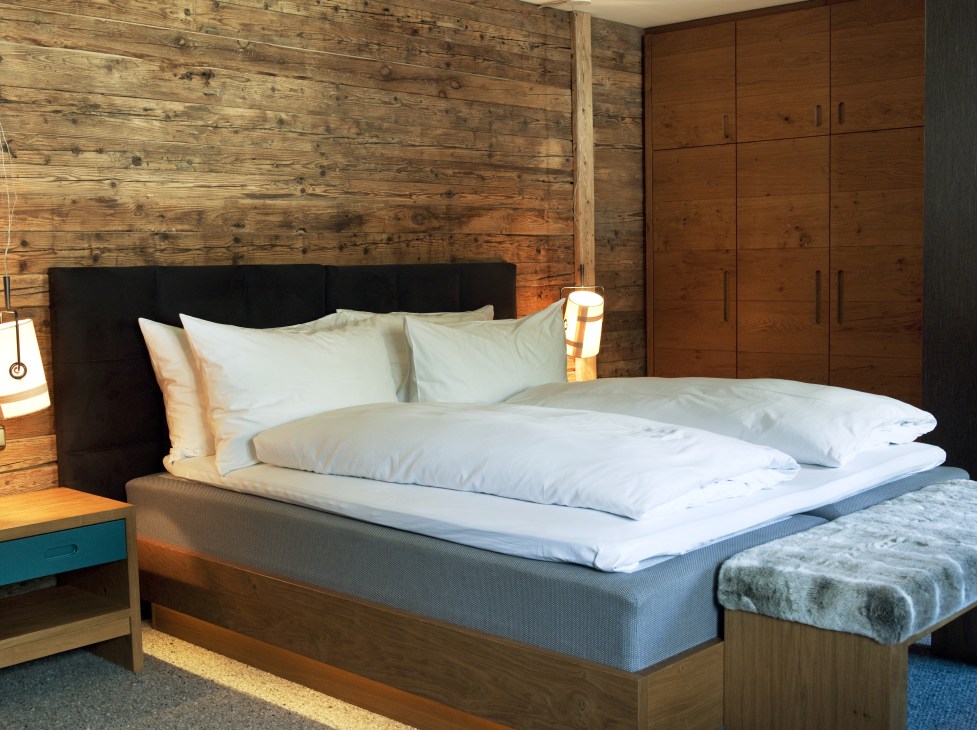 Modern hotel bedroom with wooden walls, black headboard, white pillows, and wooden wardrobe.