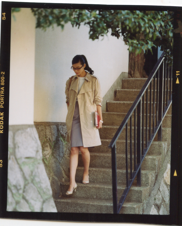Woman in Prada coat and skirt descending stone stairs in Tokyo backstreet, holding red bag.