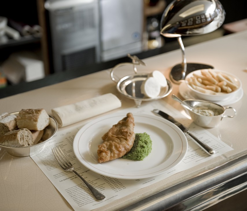 Plated haddock with bright green mushy peas at J Sheekey restaurant, served with bread and accompaniments.