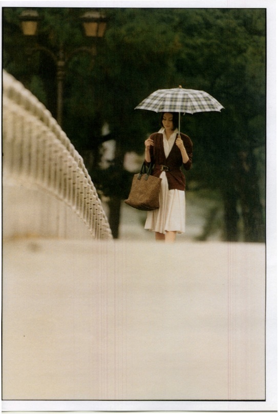 Woman holding a checkered umbrella wearing a Salvatore Ferragamo dress and Fendi cardigan in a park setting.