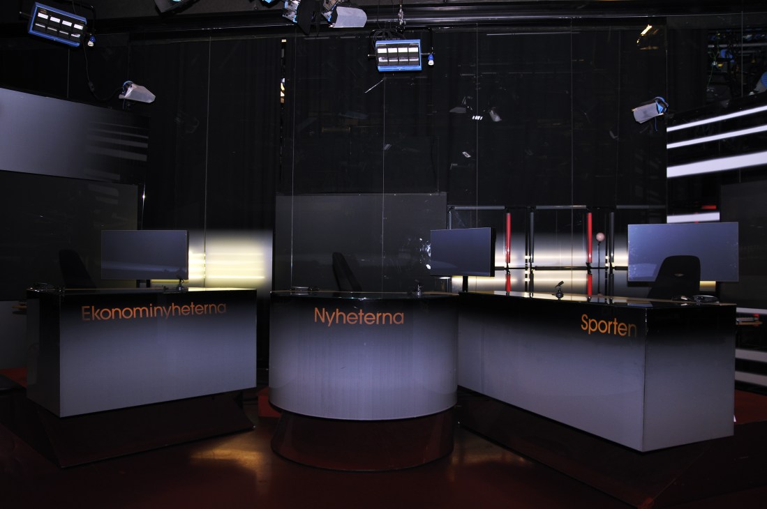 TV4 news studio with illuminated desk sections labeled in Swedish and professional lighting equipment overhead.