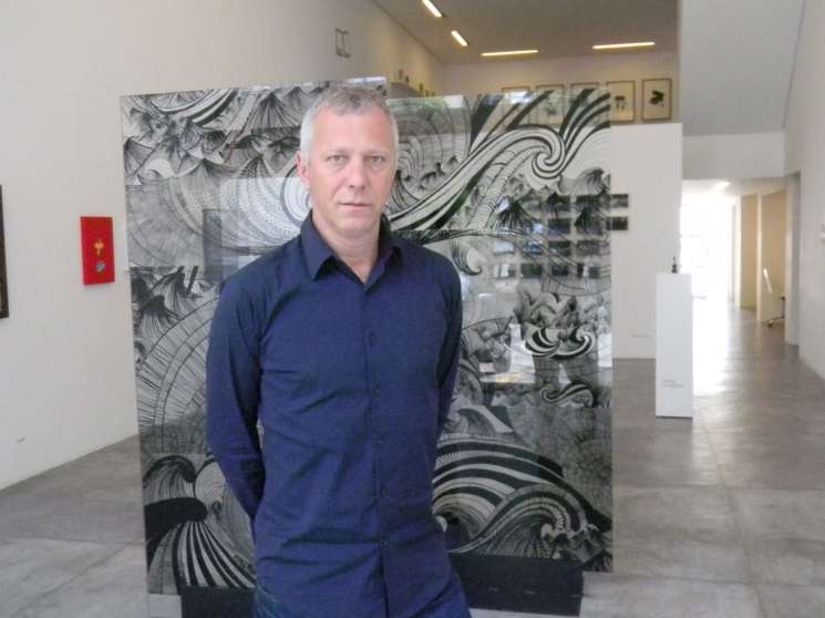Man in navy shirt standing in front of abstract black and white patterned artwork in a gallery space.