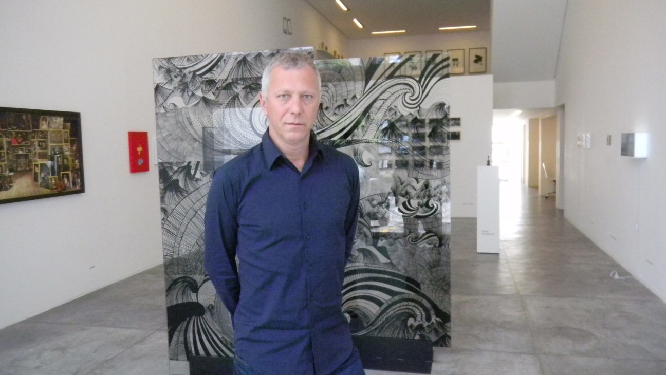 Man in navy shirt standing in front of abstract black and white patterned artwork in a gallery space.