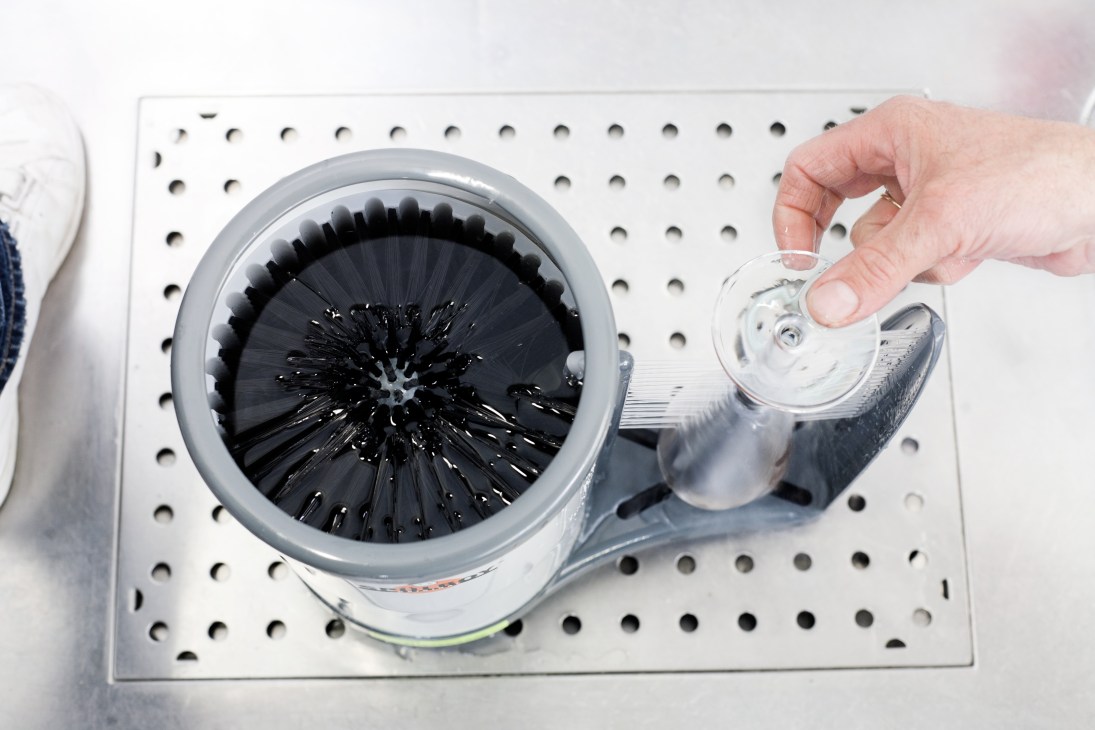 Hand demonstrating Spülboy glass washer with rotating brush mechanism and water rinse function.