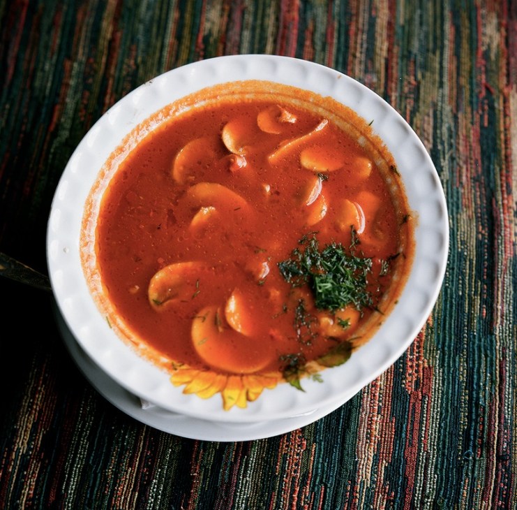 Spicy tomato soup with mushrooms served in a white bowl on a colorful striped textile.