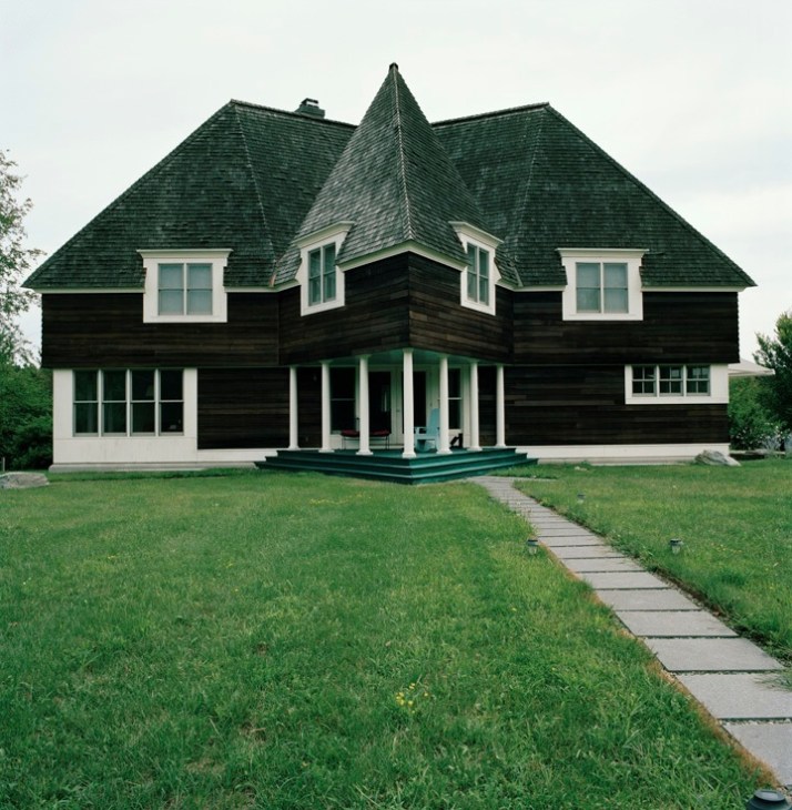 A distinctive six-point star-shaped house with black wooden exterior, white trim, and green roofing in upstate New York.