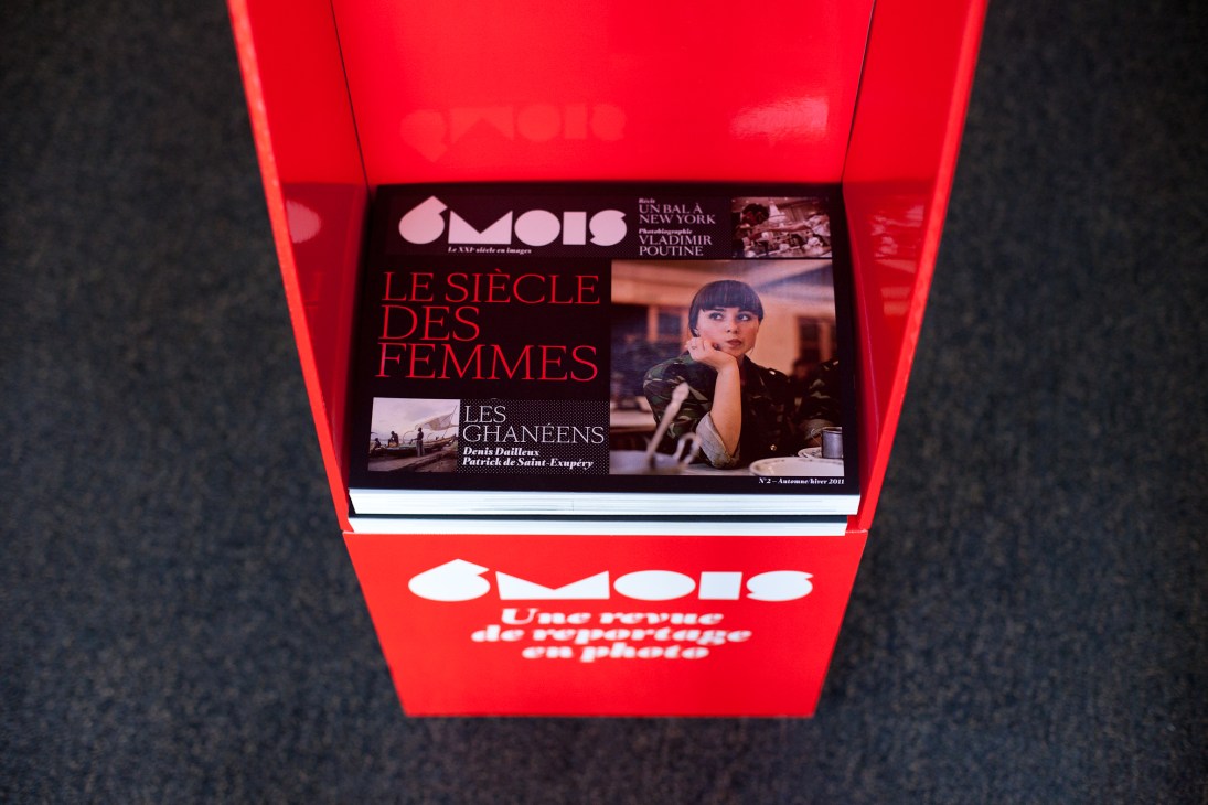 6 Mois magazine displayed in a red landscape-format holder showing its cover featuring women and French text.