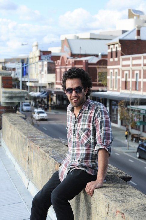 Mike O'Hanlon, owner of The Bird and Ezra Pound bars, sits on a waterfront wall overlooking Northbridge's heritage buildings.