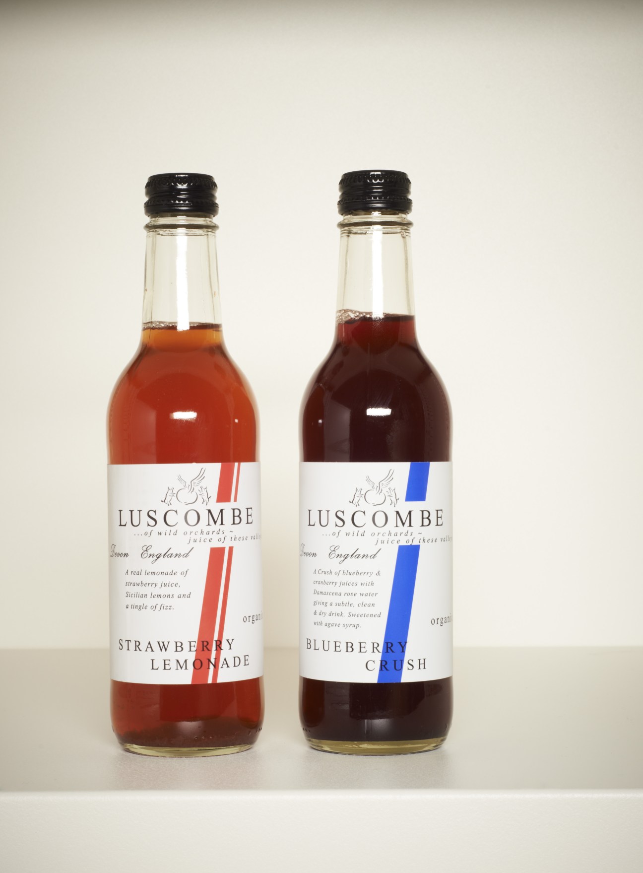 Two Luscombe glass bottles of fruit drinks - strawberry lemonade and blueberry crush.
