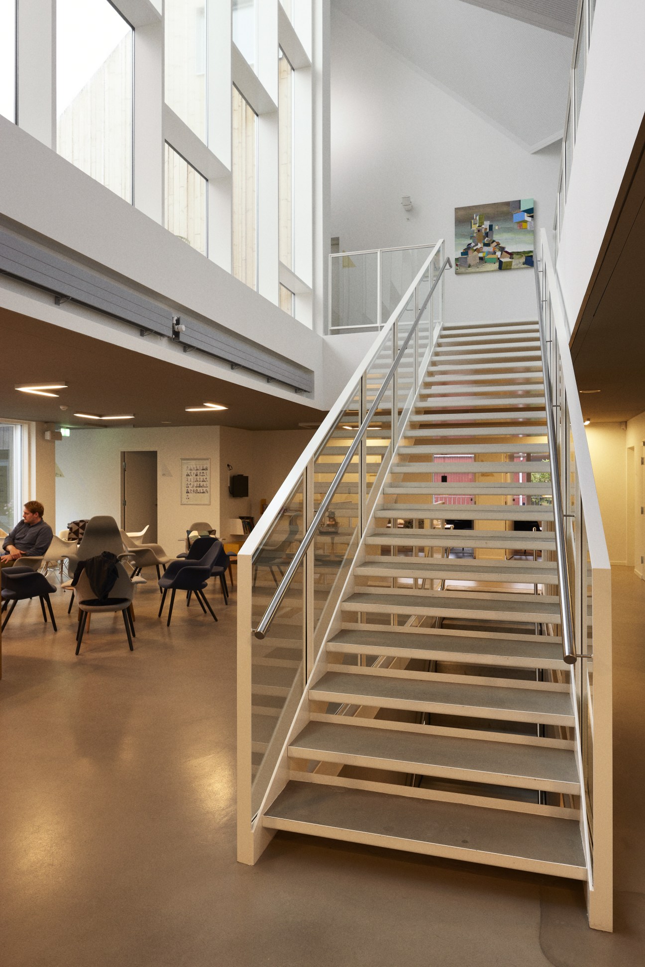 Bright stairway with wooden steps and metal railings leading to first floor, with lounge seating area below.