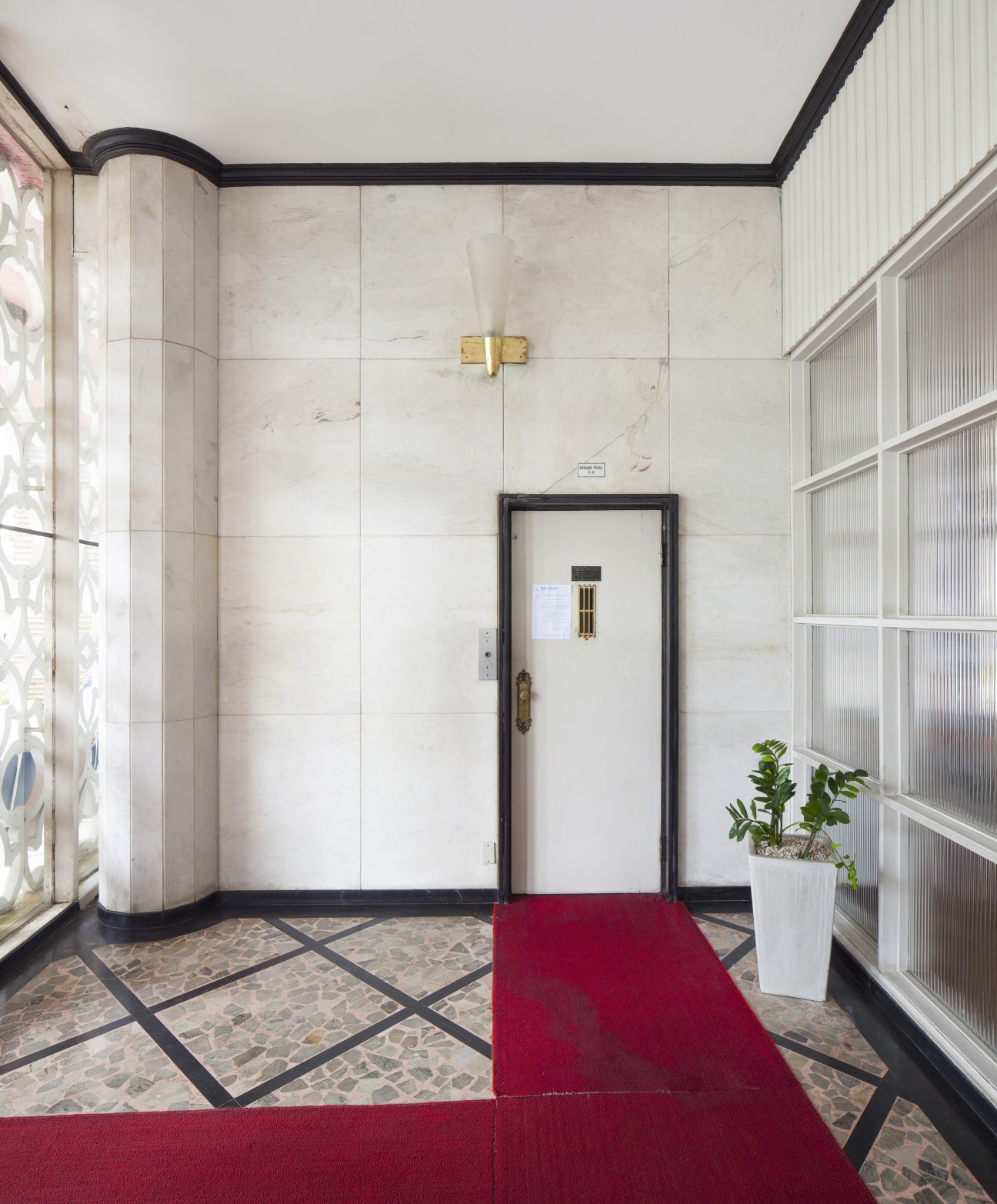 Art Deco lift entrance with marble walls, brass fixtures, and red carpet runner in Parque Verde Mar.
