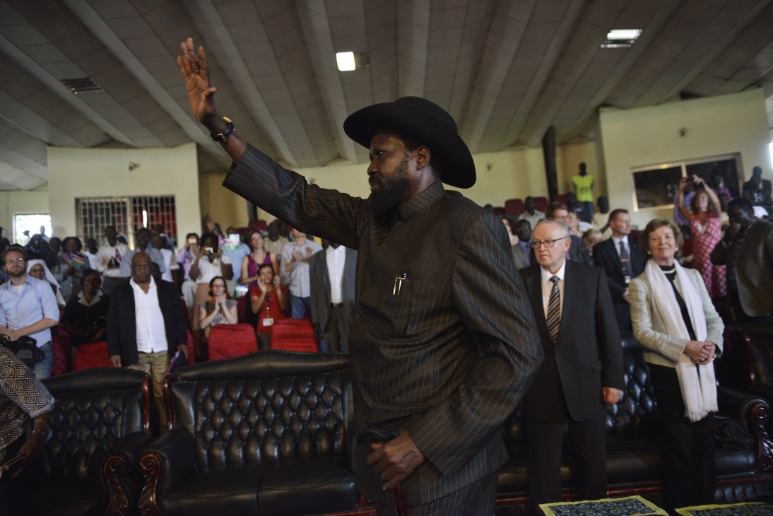 South Sudan president Salva Kiir in a dark pinstriped suit and cowboy hat waves to a crowd gathered in an indoor venue.