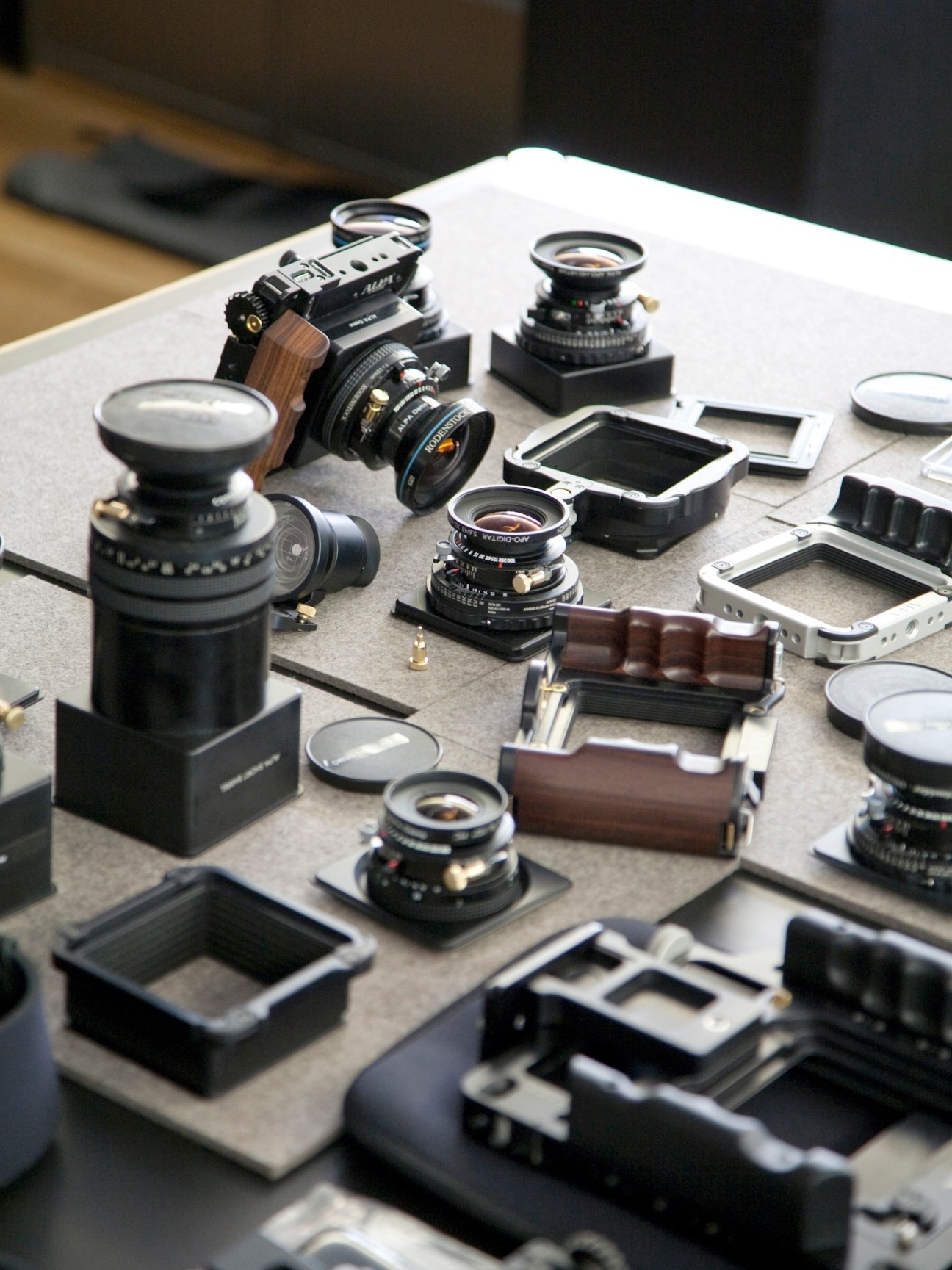Alpa 12 cameras and lenses displayed on a table, including camera bodies with rosewood handgrips and various lens attachments.