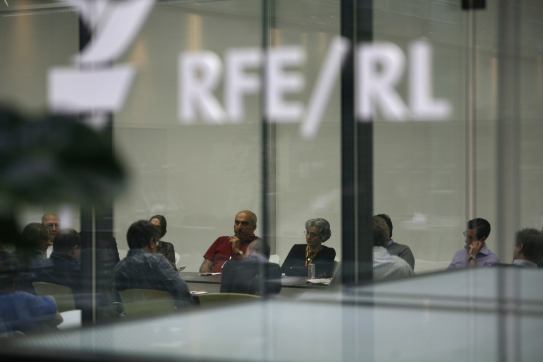RFE/RL staff members in a meeting room with the organization's logo visible on glass wall.