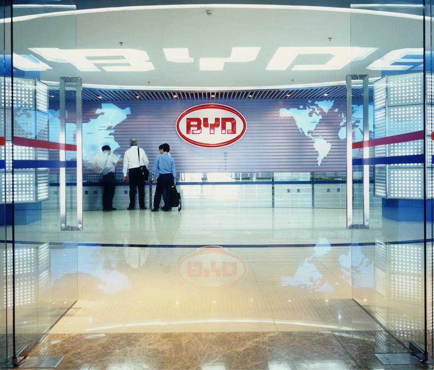 BYD entrance lobby with red oval logo and world map, employees standing at reception desk.