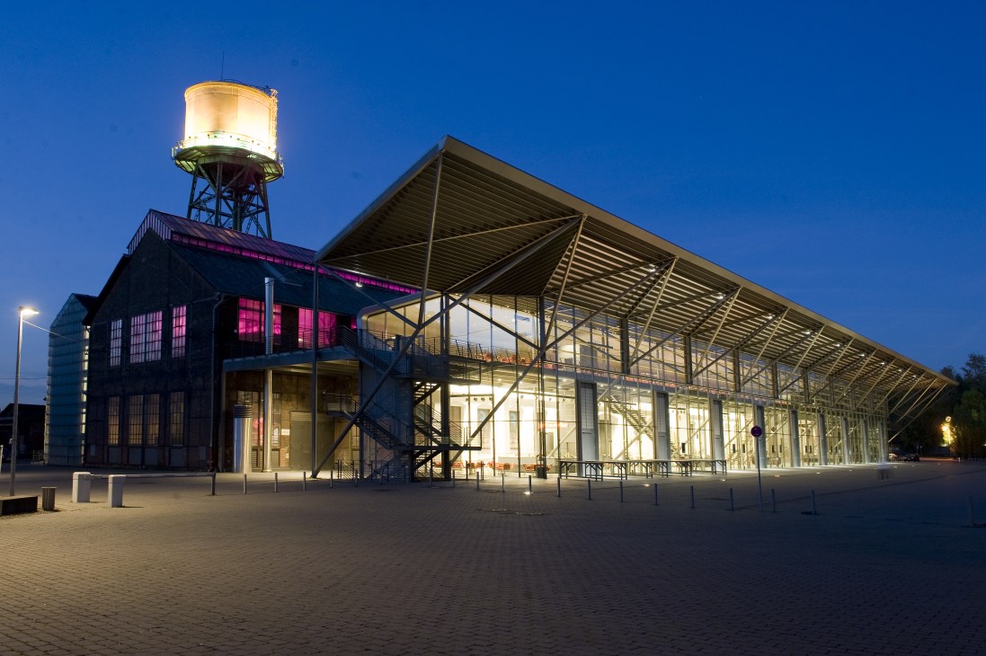 Illuminated Jahrhunderthalle conference centre at dusk with converted power station architecture and vintage water tower.