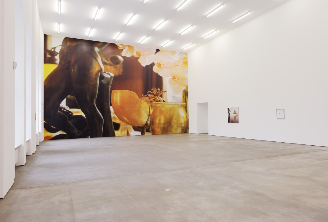 Louise Lawler exhibition with large-scale photograph on gallery wall featuring golden tones and orchids.