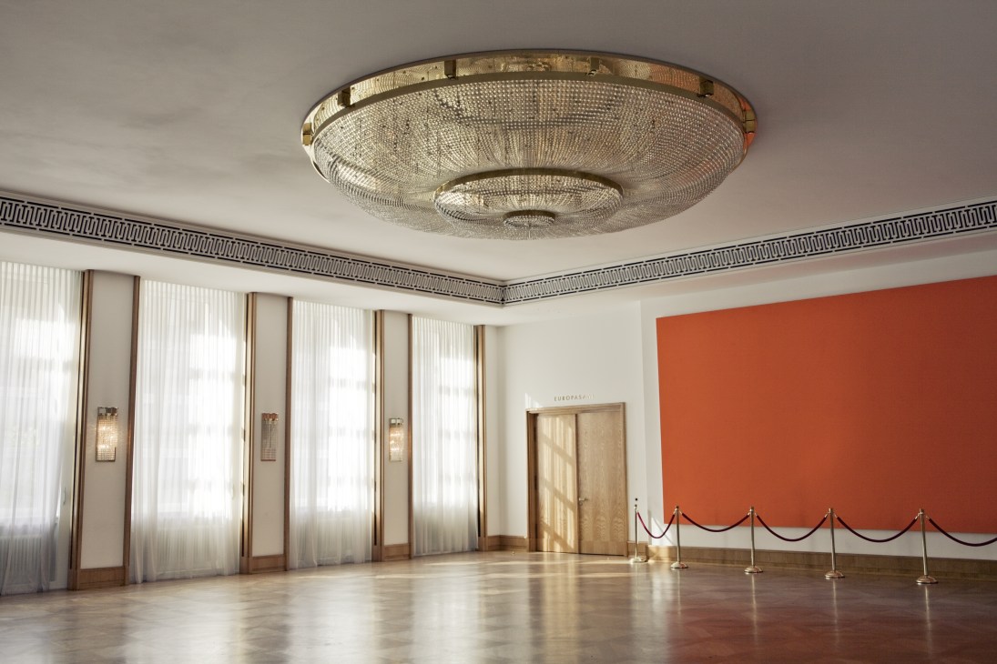 Entrance hall with art deco ceiling fixture, striped wall trim, ochre wall panel and velvet rope barriers.