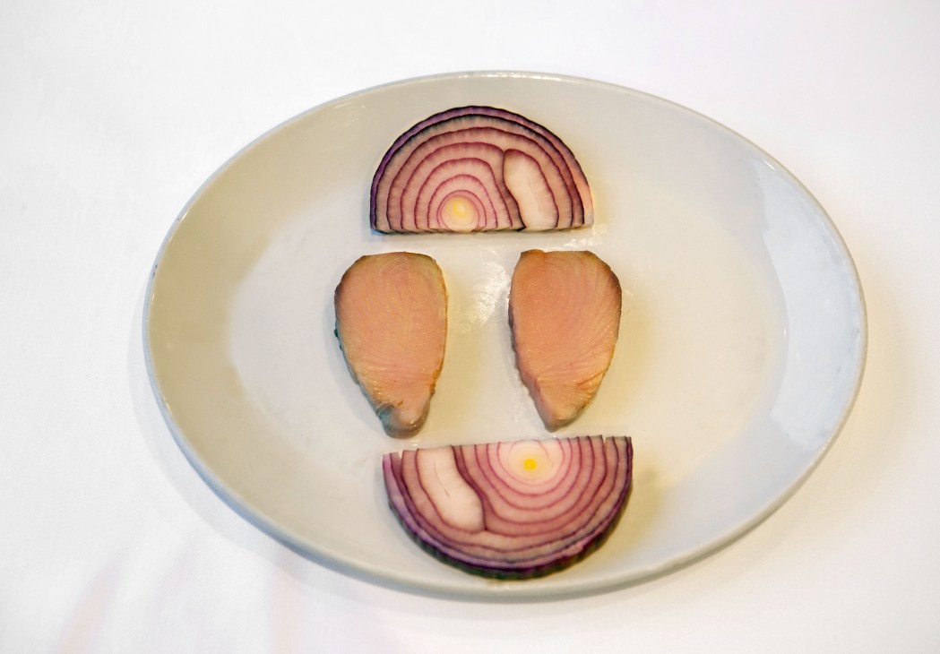 Sliced red onions and salmon-colored lakerda arranged on a white plate to form a face.