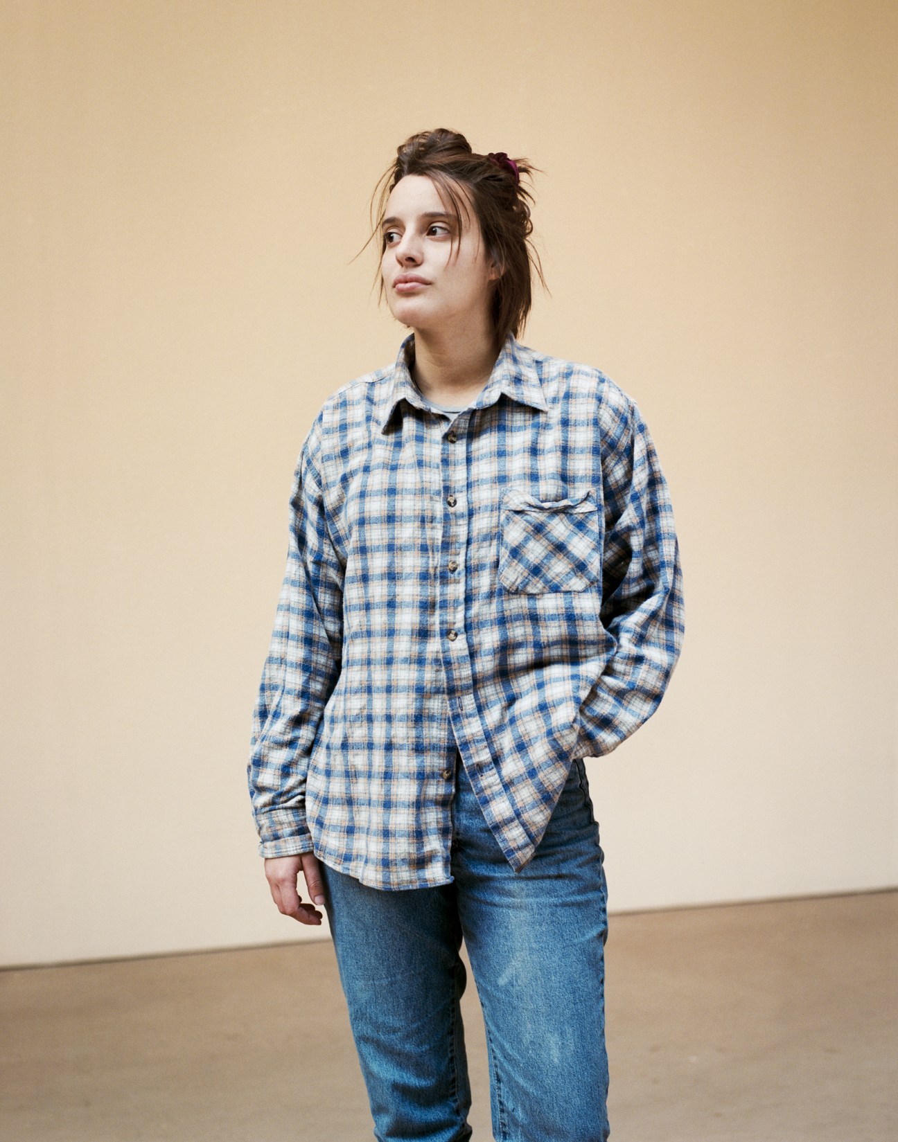 Portrait of Catarina Cubelo, a BA Fine Art student from Portugal, wearing a blue plaid shirt and jeans against a neutral background.