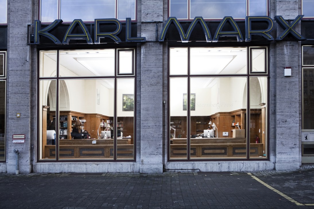 Sternberg Press storefront in the former Karl Marx Buchhandlung building with illuminated signage and wooden interior visible through large windows.