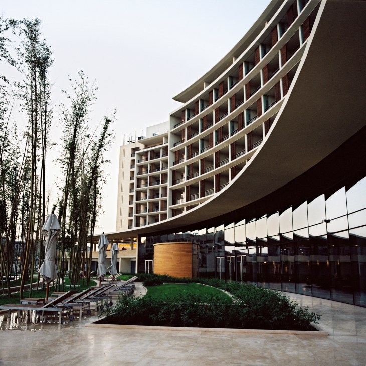 Hotel Kempinski's curved facade with multiple balconies overlooking a courtyard with bamboo trees and parasols.