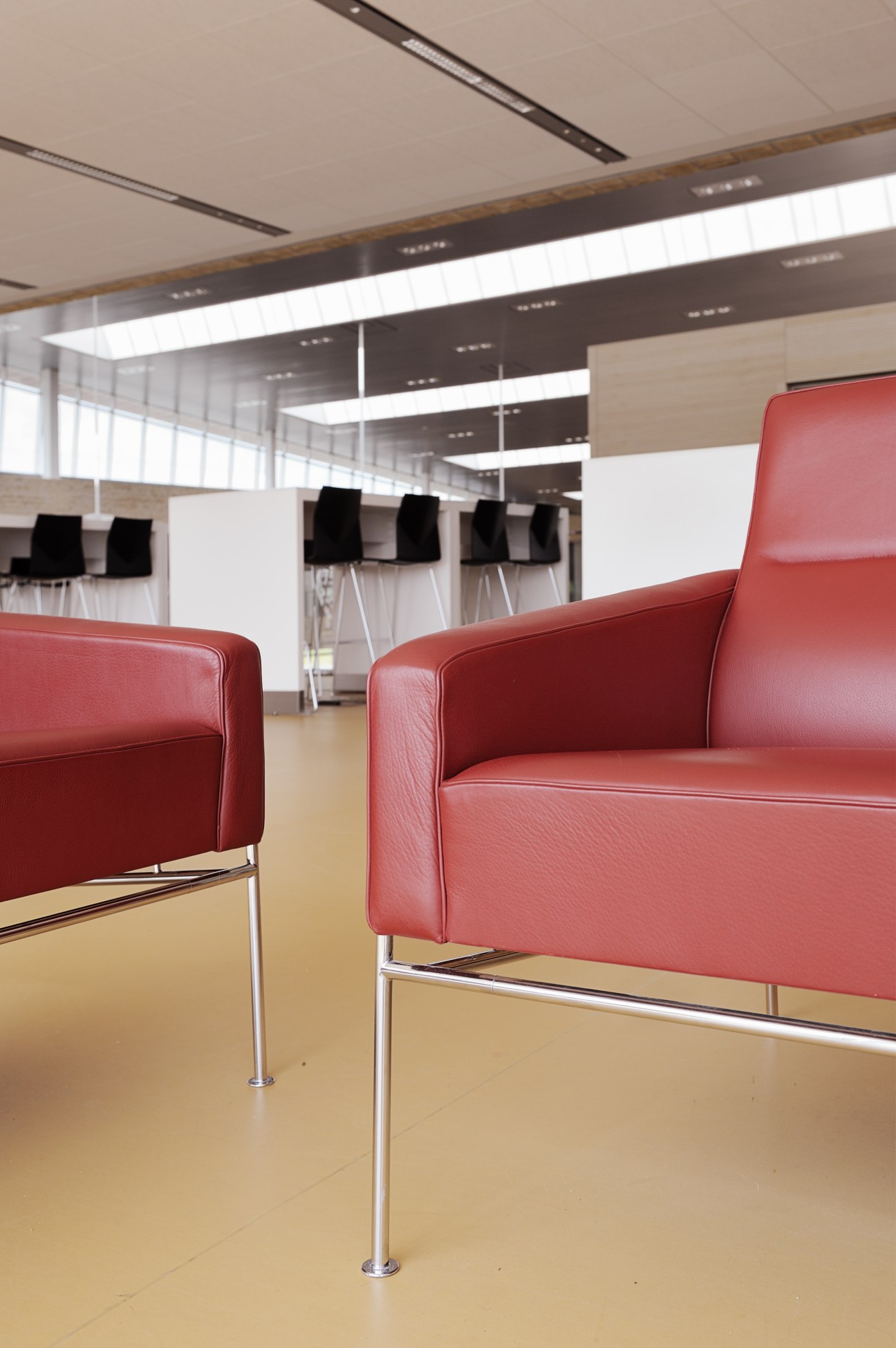 Red Arne Jacobsen chairs in a bright, minimalist interior space with skylights and black chairs in the background.