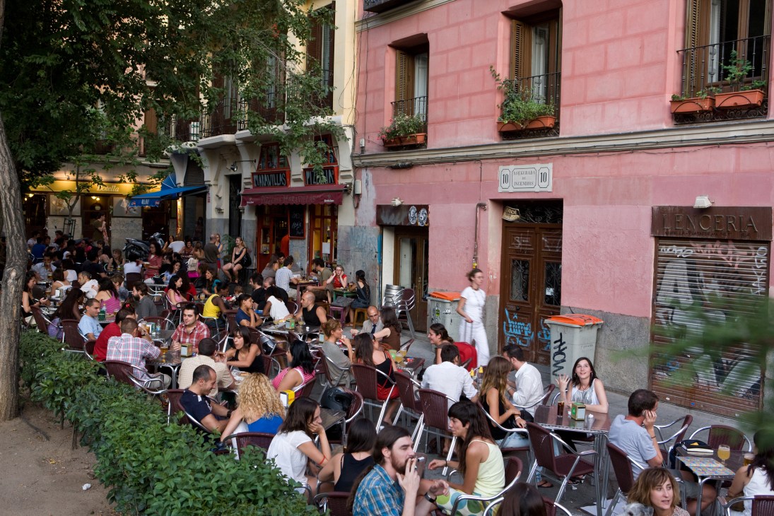 Crowded outdoor terrace of Pizzeria Maravillas in Madrid with diners seated at tables on a tree-lined street.