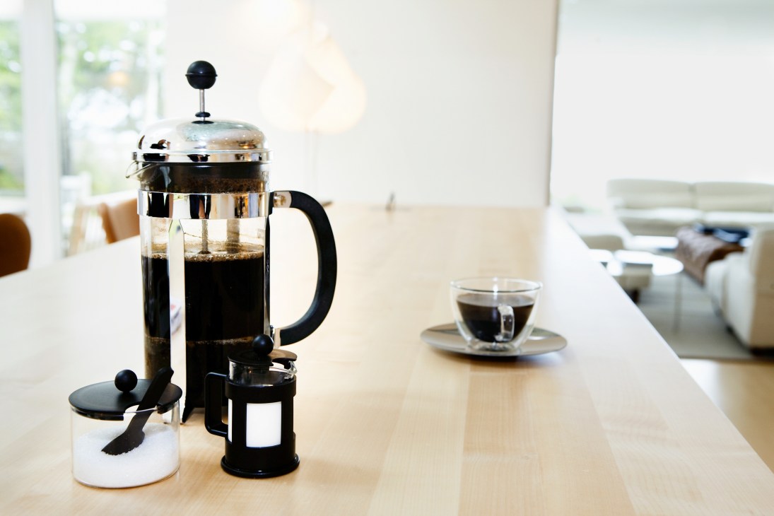 A Bodum French press coffee maker with brewed coffee on a wooden table next to a cup.
