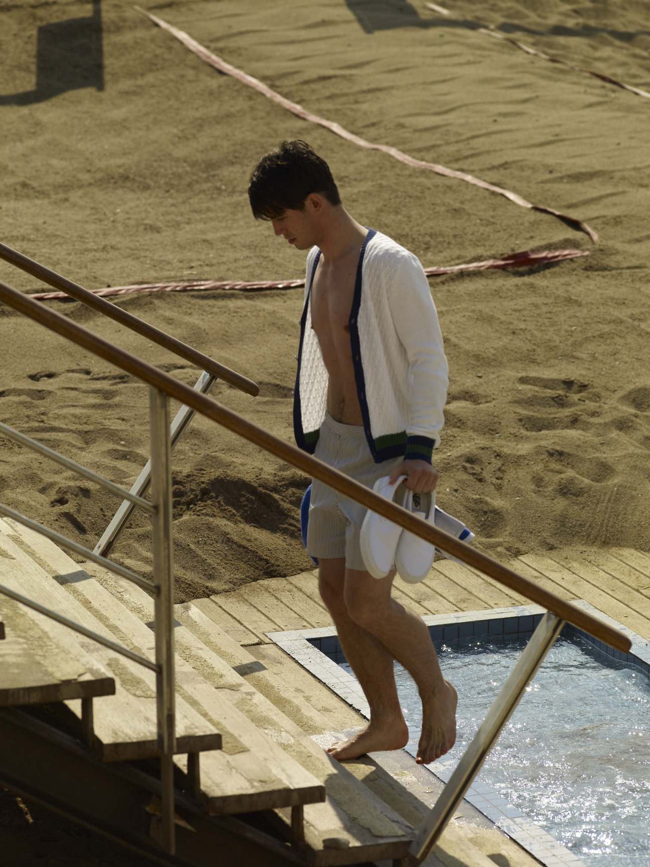 Man wearing white swimming shorts and cardigan on beach stairs at Barcelona swimming club.