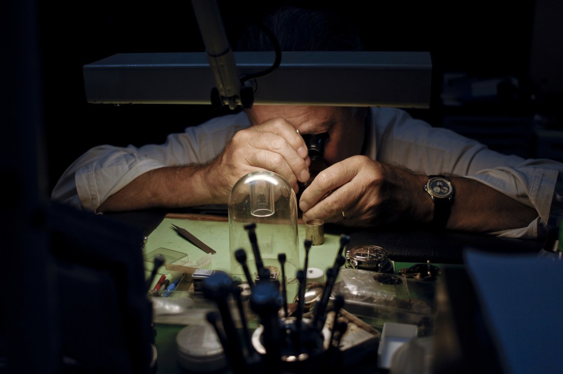 A watchmaker's hands working under a magnifying lamp on a luxury watch mechanism at L'Elysée in Buenos Aires.