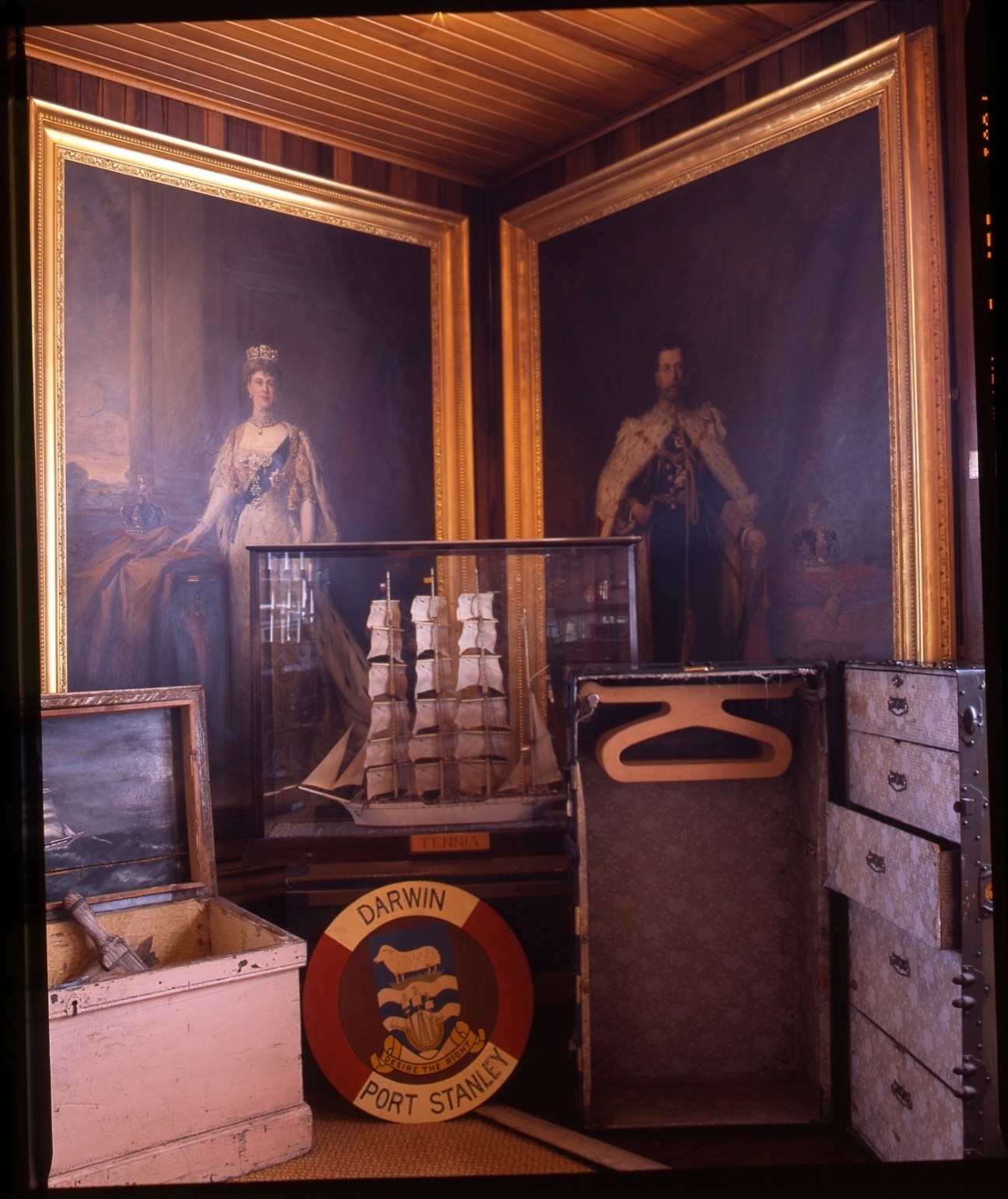 Museum display with Royal portraits and ship model behind glass, with Darwin Port Stanley emblem visible.