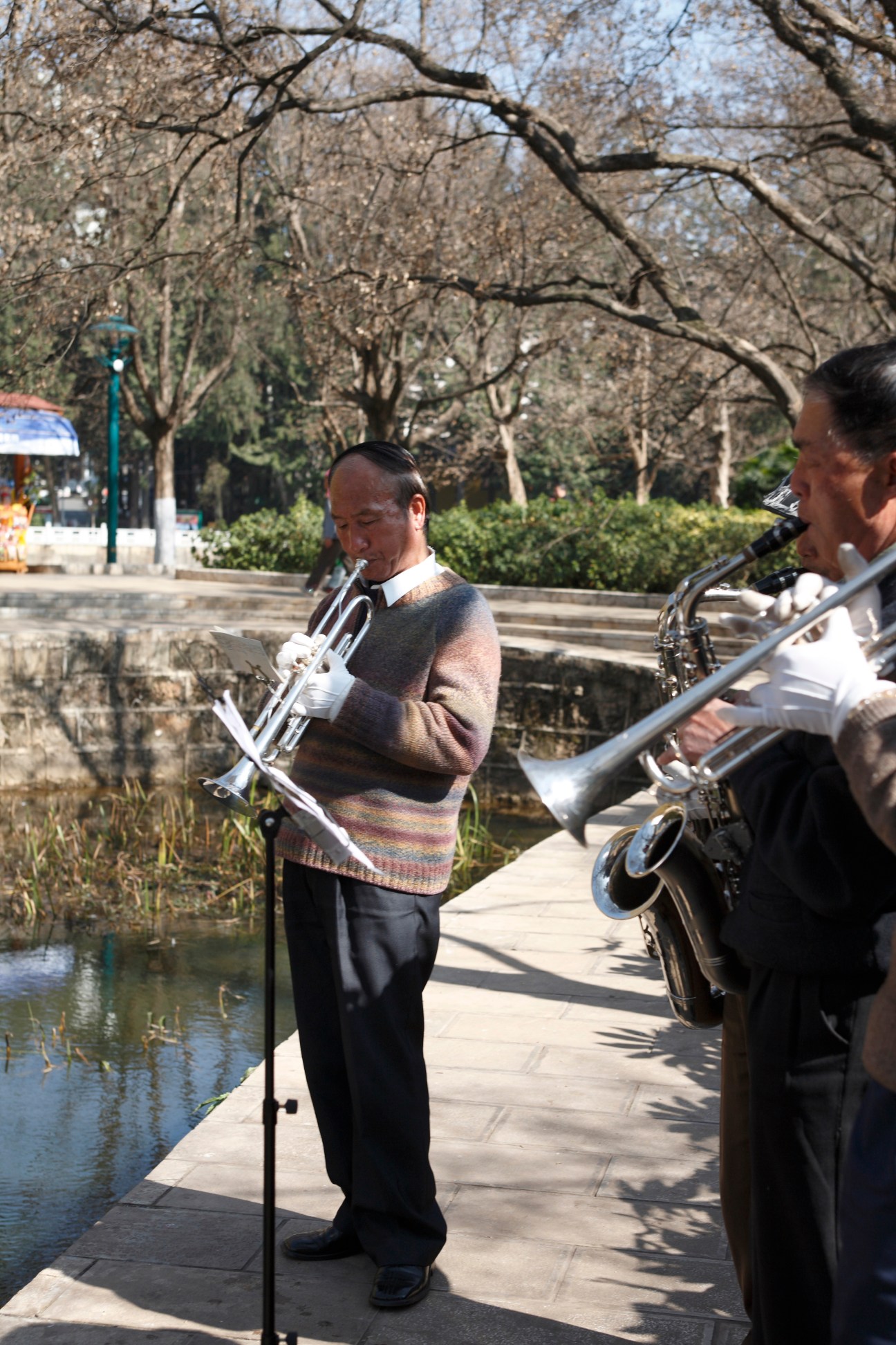Two musicians playing brass instruments by the water at Green Lake in Kunming.