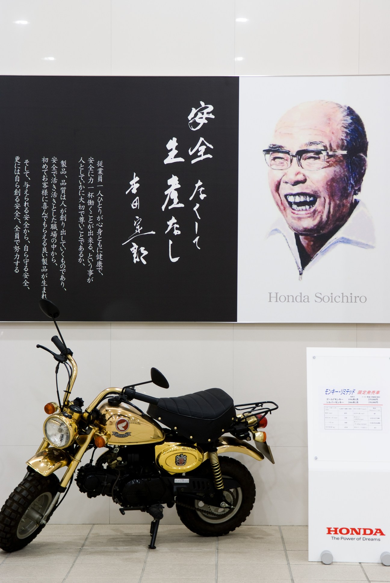 Limited-edition gold Honda Monkey bike displayed beneath a wall portrait of founder Soichiro Honda with Japanese calligraphy.