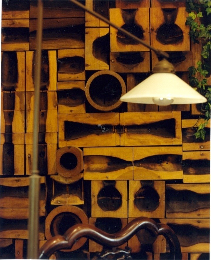 Old wooden glass moulds displayed on a wall with a modern pendant light.