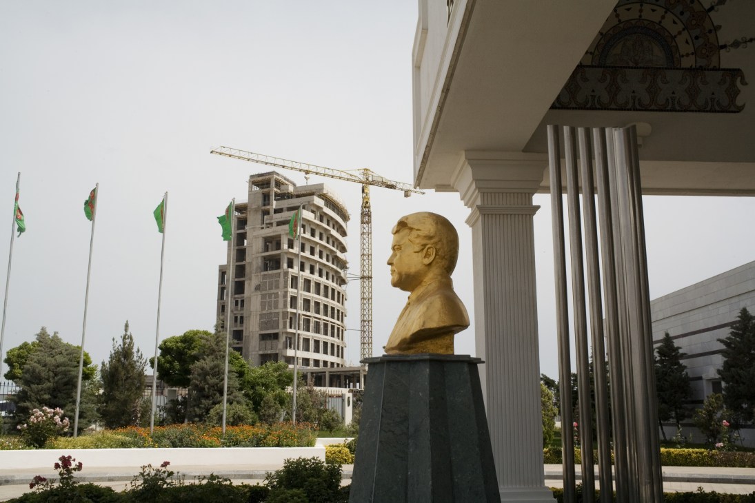Golden bust of former president Niyazov at Hotel Serdar in Avaza resort with construction cranes and flags in background.
