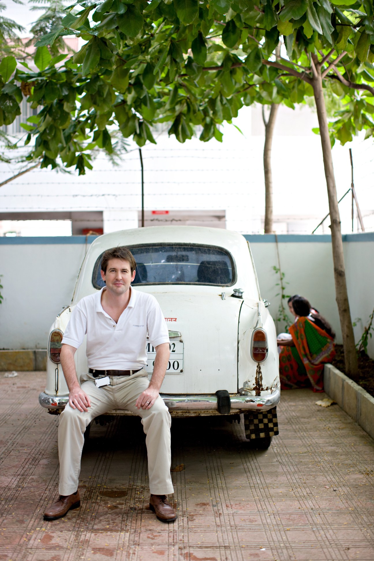 John Roebuck, a British engineer, sits on the bumper of a vintage white Fiat car in Pune.