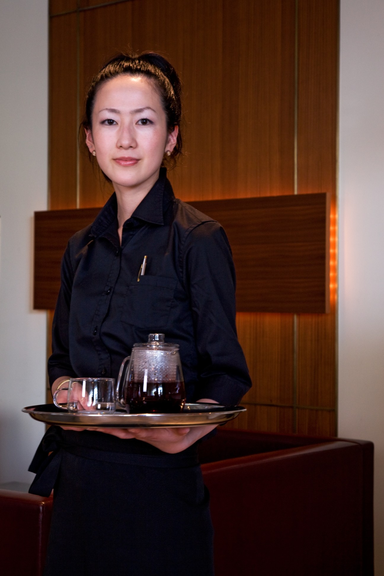 Woman in black shirt serving tea at Kiokuh restaurant with wooden interior backdrop.