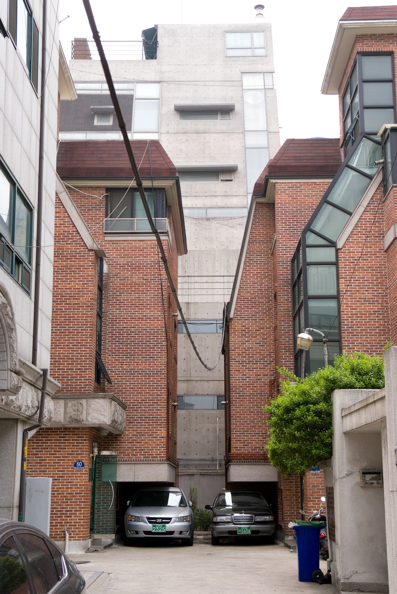 Modern apartment buildings with brick and concrete facades, parked cars in courtyard below.