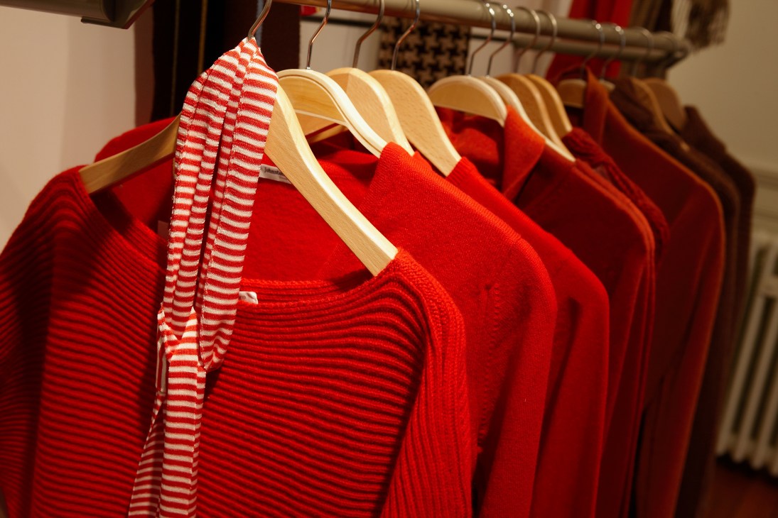 Red and striped cashmere sweaters hanging on wooden hangers at Johnstons Cashmere factory in Scotland.