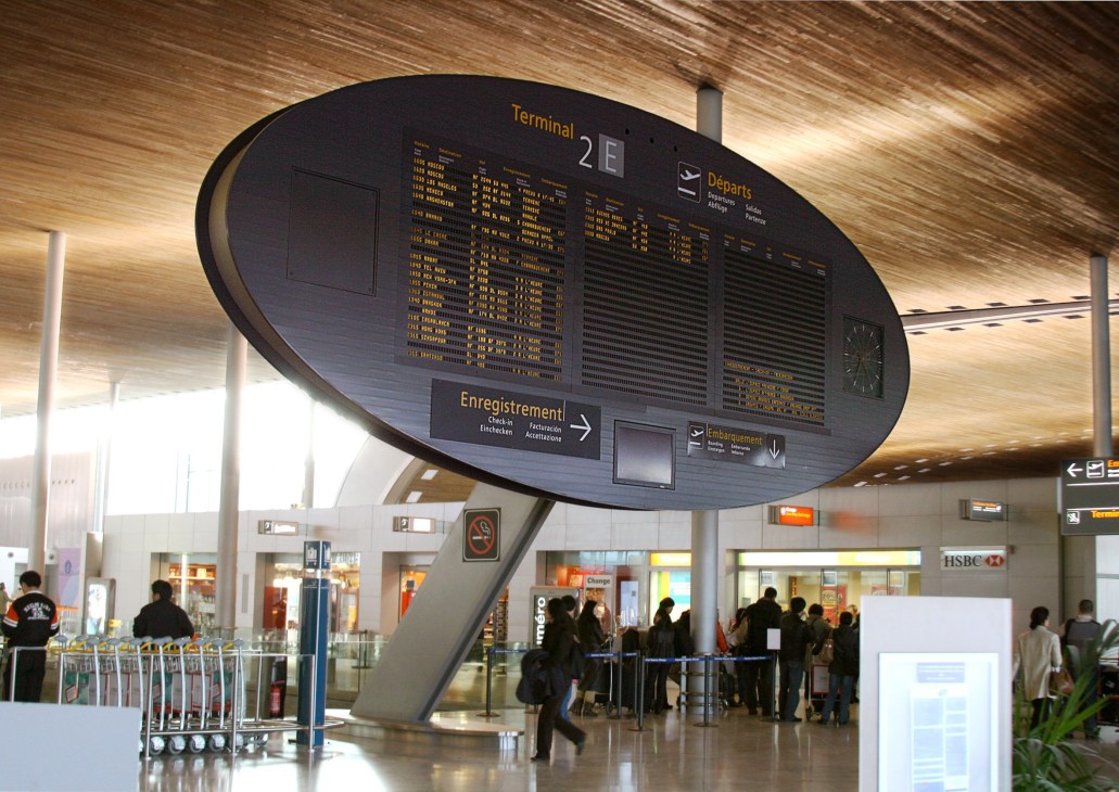 Large oval airport information display board showing flight departures at Charles de Gaulle airport terminal.