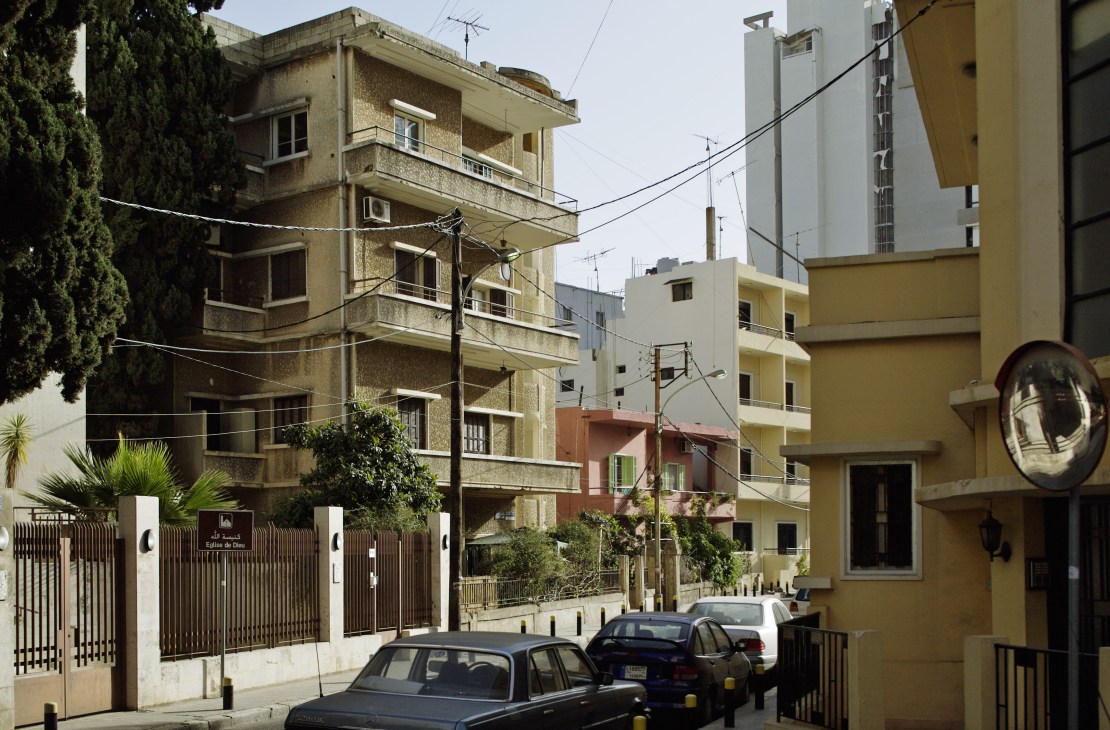 Street scene in Ashrafieh showing older residential buildings mixed with newer yellow structures and parked cars.
