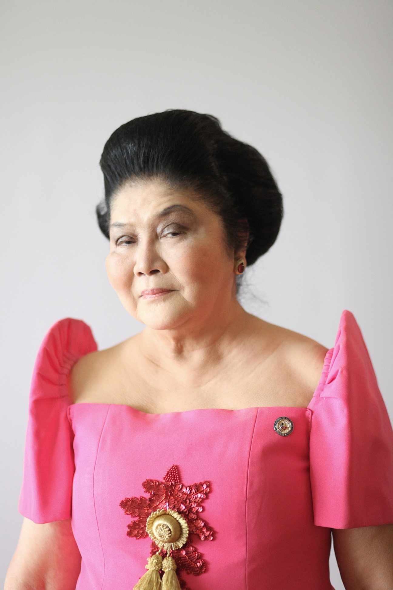 Imelda Marcos wearing a pink off-shoulder gown with dramatic ruffled sleeves and ornate gold embellishments.