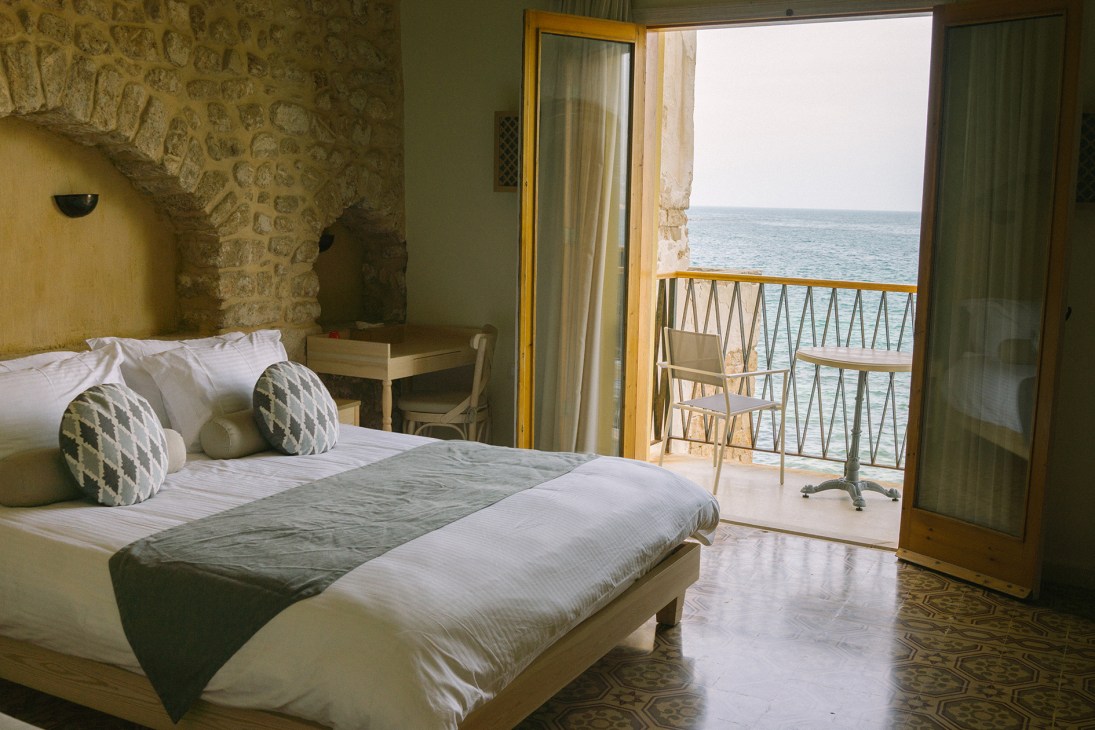 Bedroom at Dar Alma with stone walls, sea-view balcony and Mediterranean vista.