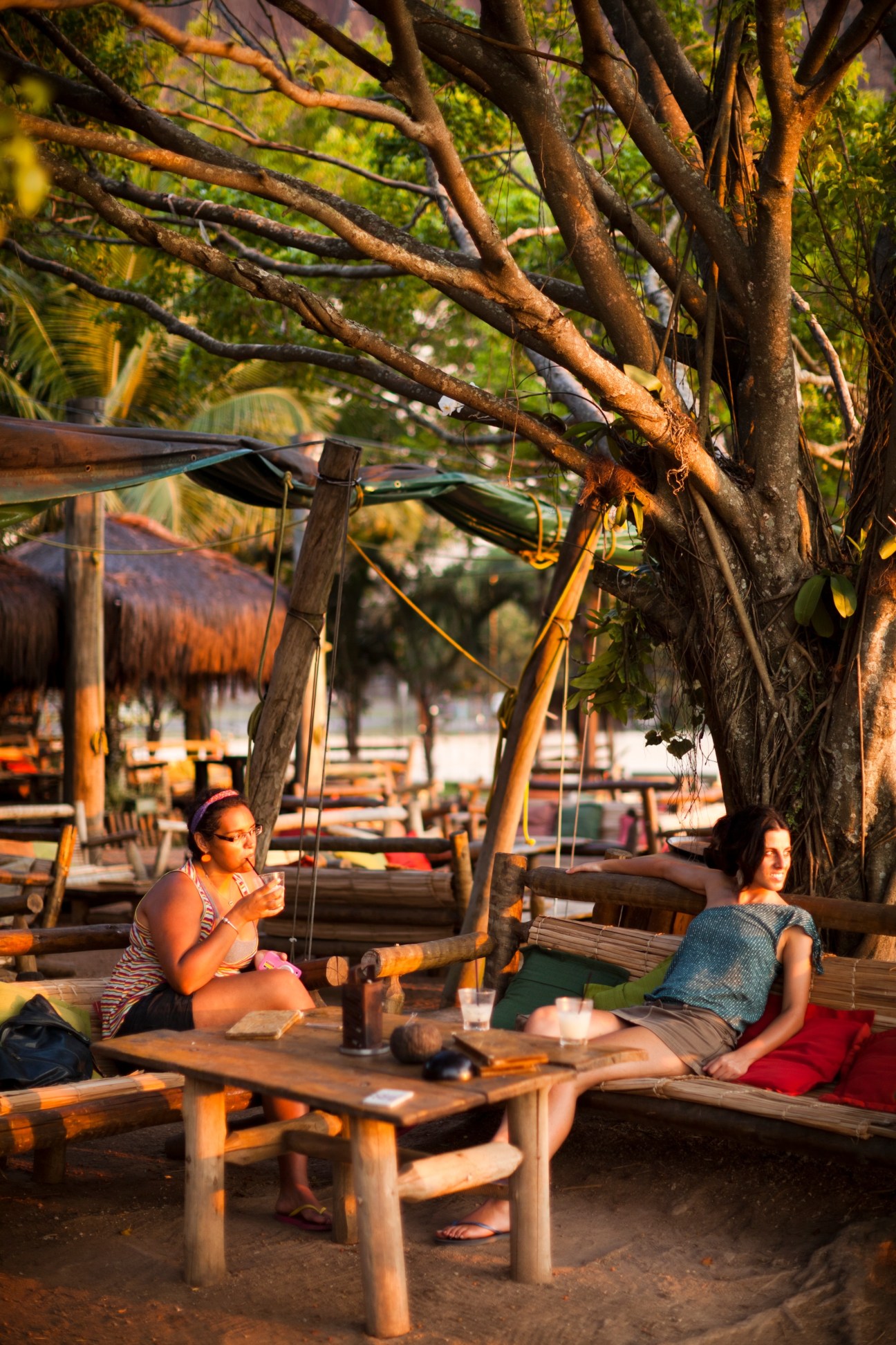 Two women sitting under a large tree at Palaphitas Kitch bar in Rio, watching the sunset over the lagoon.