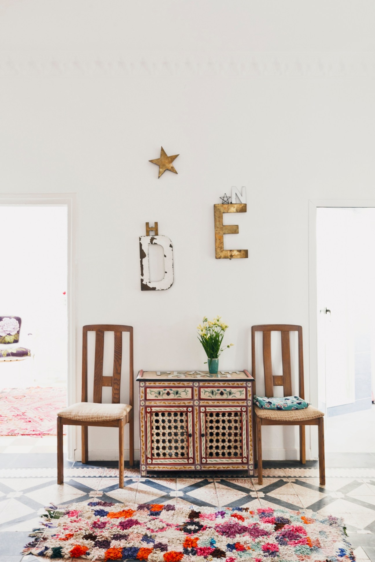 Julie Klear's living room with eclectic décor including wooden chairs, decorative wall letters, and a colorful patterned rug.