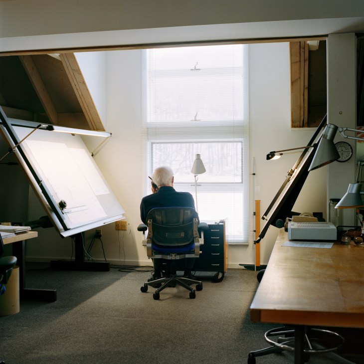 Niels Diffrient seated at his drawing board in his Connecticut studio, gazing out a large window toward the countryside.